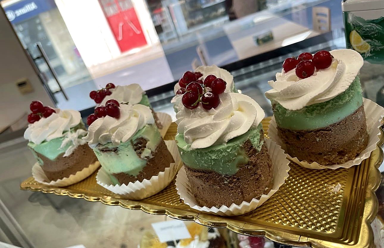 Doces individuais com creme verde, chantilly e groselhas, num tabuleiro dourado